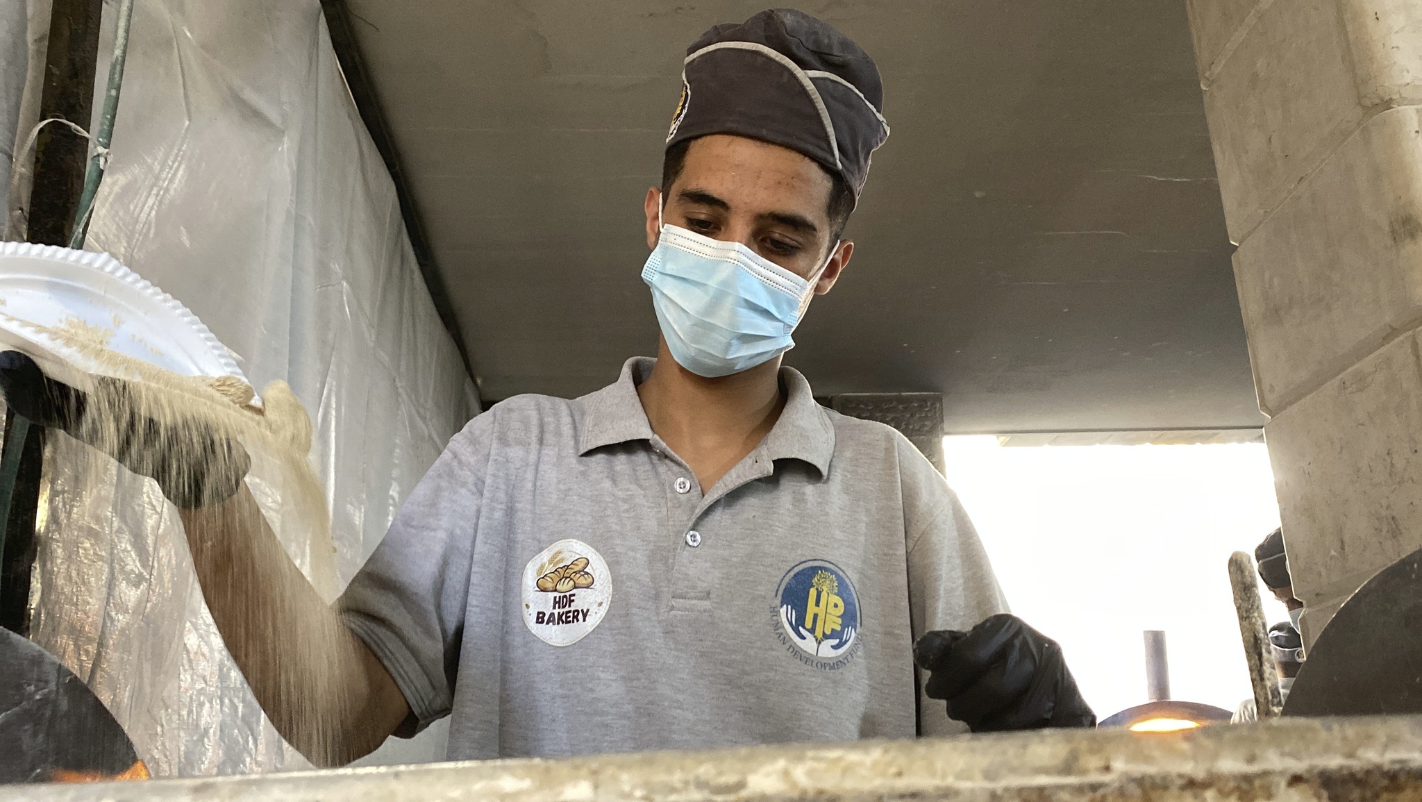 An HDF bakery worker scatters flour onto the work surface as he prepares bread in Gaza
