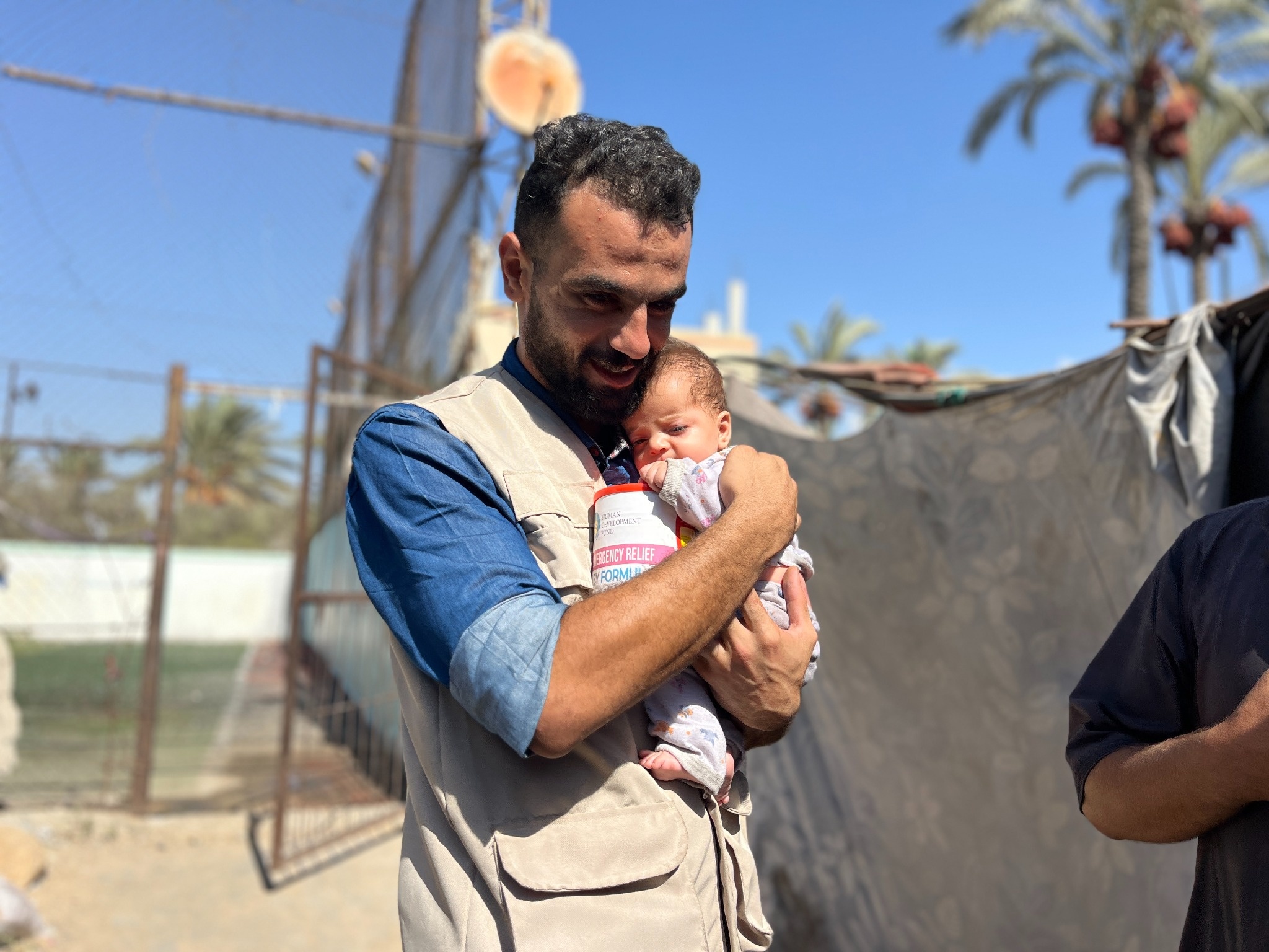 An HDF team member holds a baby and a container of emergency infant formula in Gaza