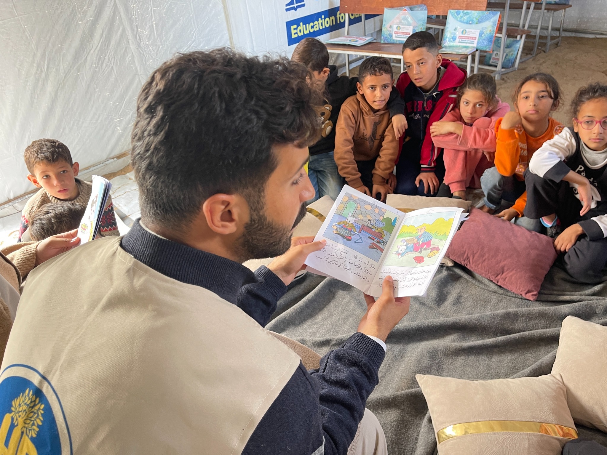 An HDF team member reads an illustrated book to a group of children seated together in a classroom