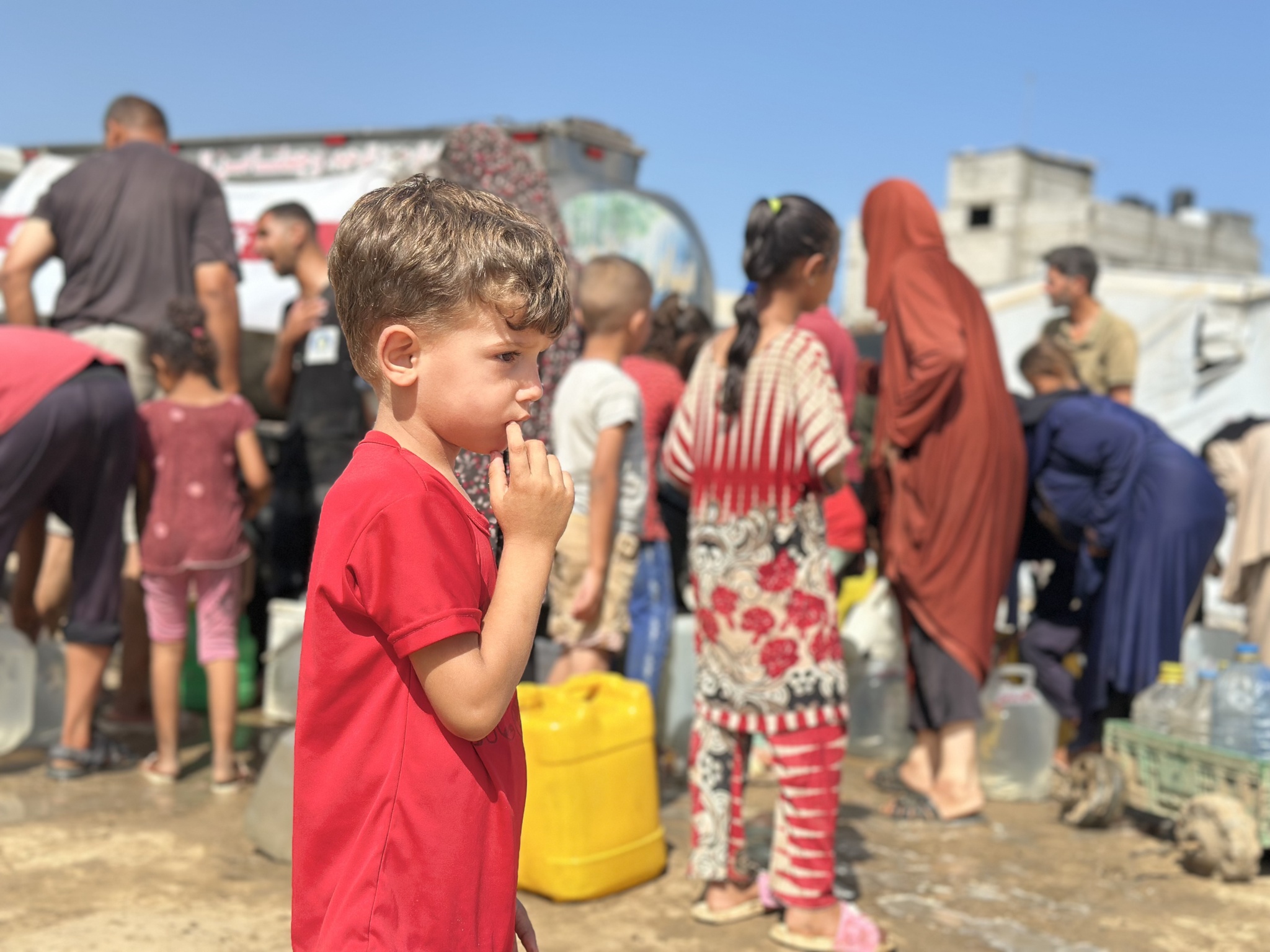 A boy stands in the foreground while families collect water beside a tanker in Gaza